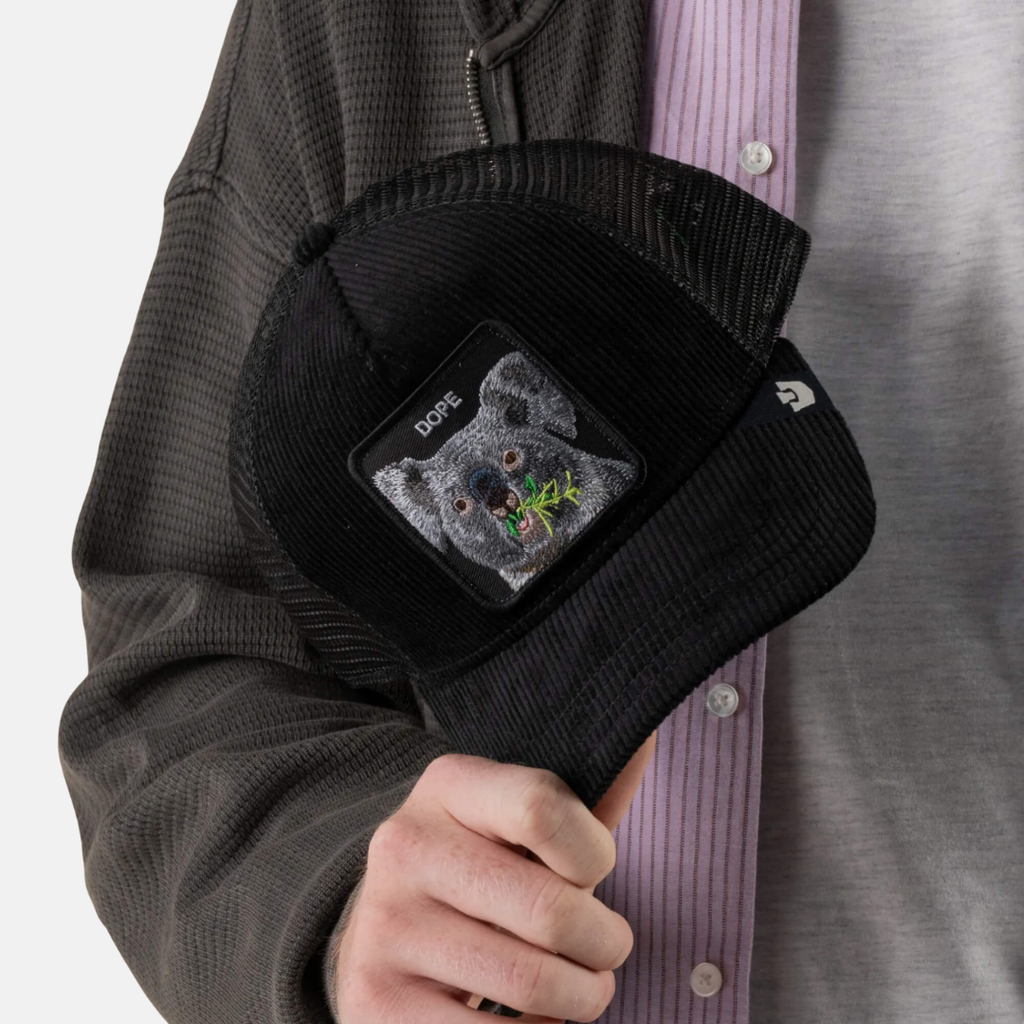A person wearing a black corduroy cap with a square patch featuring a dog's face and the word 'DOGS'.