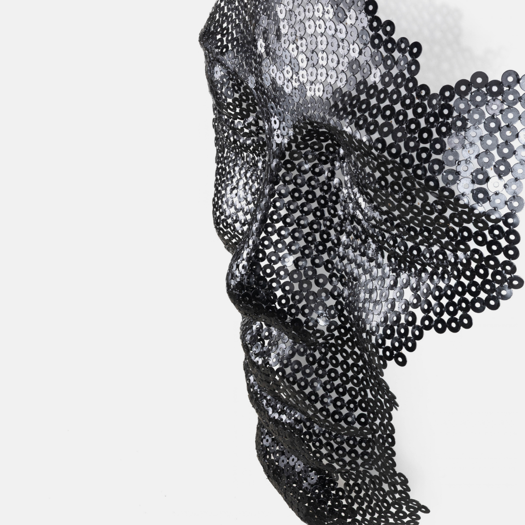 A close-up side profile of a sculptural face made of black and silver sequins on a plain light gray background.