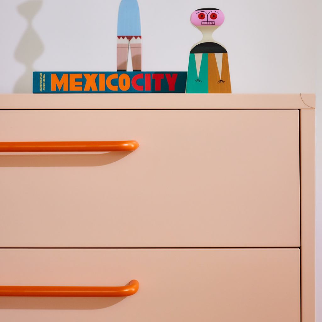 Beige dresser with orange handles featuring a 'Mexico City' book and colorful figurine on top.